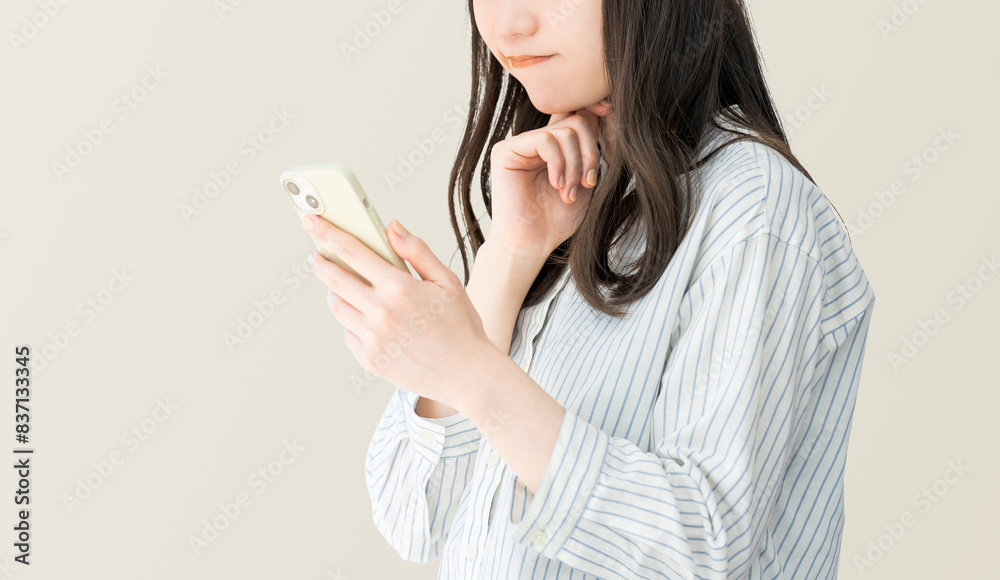 スマートフォンを見て考える若い日本人女性・ビジネスウーマン スマートフォンを見て考える若い日本人女性・ビジネスウーマン