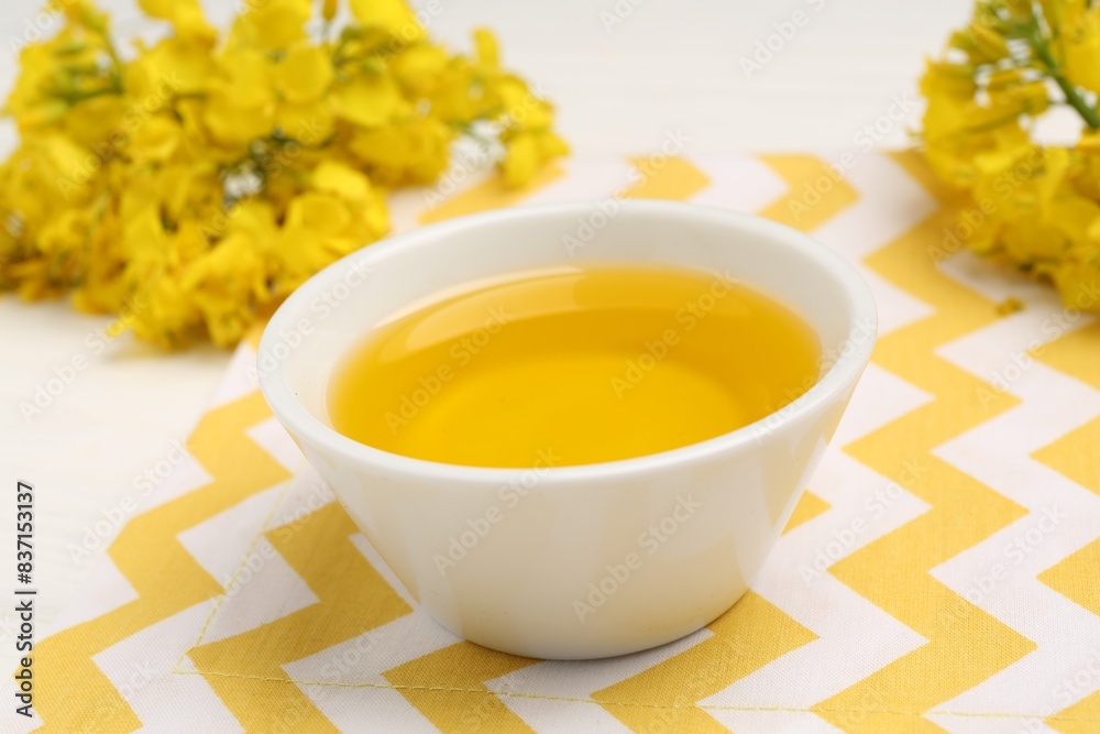 Rapeseed oil in bowl and beautiful yellow flowers on table, closeup Rapeseed oil in bowl and beautiful yellow flowers on table, closeup