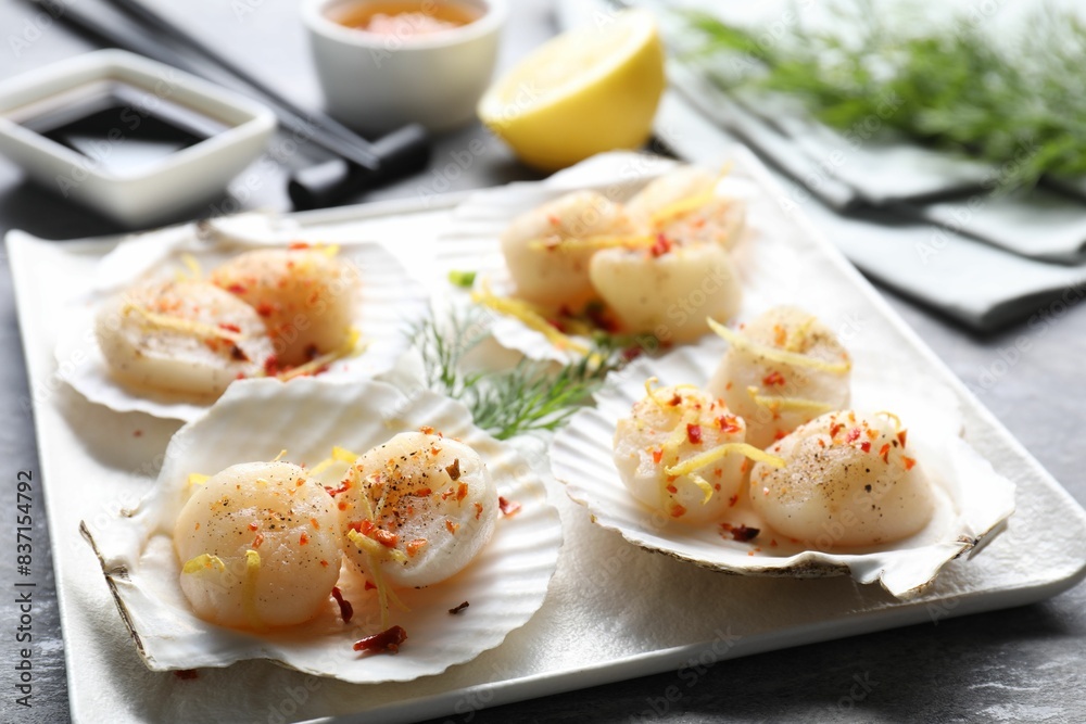 Raw scallops with spices, lemon zest and shells on grey table, closeup Raw scallops with spices, lemon zest and shells on grey table, closeup