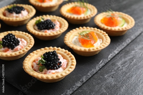 Delicious canapes with salmon and caviar on black textured table, closeup
