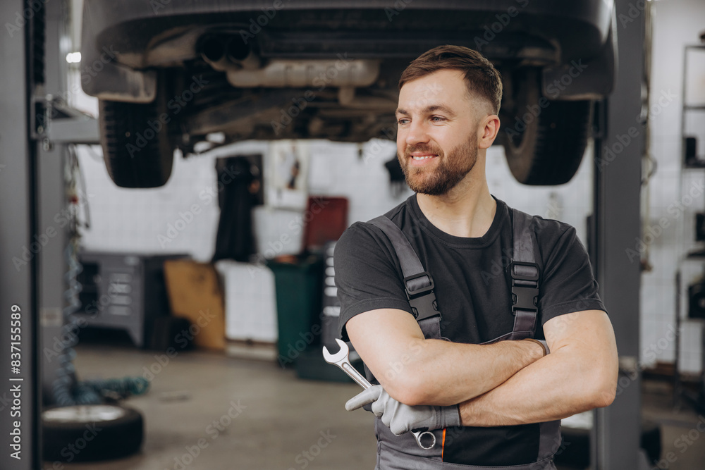 Smiling bearded mechanic while standing with crossed arms and holding wrenches in a car service Smiling bearded mechanic while standing with crossed arms and holding wrenches in a car service