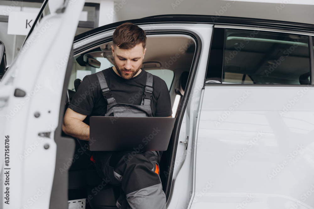 Automotive mechanic running diagnostics software on computer. Mechanic sitting in car and working on laptop while doing vehicle diagnostic test in auto service garage. Automotive mechanic running diagnostics software on computer. Mechanic sitting in car and working on laptop while doing vehicle diagnostic test in auto service garage.