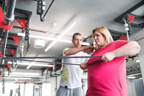 Overweight woman exercising in gym. Personal trainer couching her and helping her.