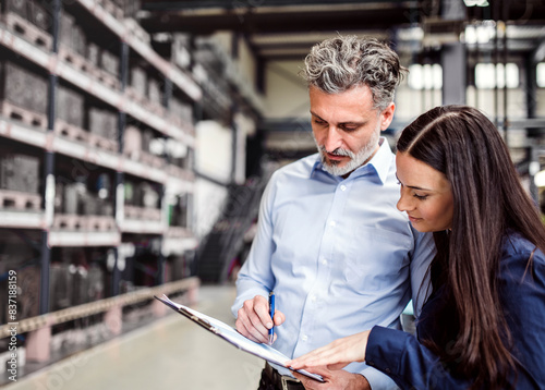 Two project managers standing in modern industrial factory. Manufacturing facility with robotics, robotic arms and automation. Storing products and materials in warehouse. photo