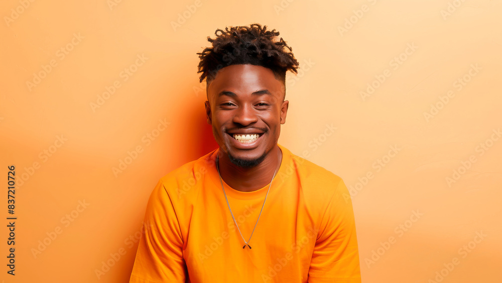 Fototapeta premium Portrait of a young man in casual clothing smiling against an orange background. Bright and cheerful imagery showcasing happiness and modern style.