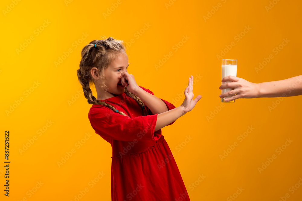 Kid girl with dairy allergy showing stop gesture front glass of milk on yellow background. Lactose intolerance concept Kid girl with dairy allergy showing stop gesture front glass of milk on yellow background. Lactose intolerance concept