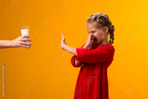 Fotografía Kid girl with dairy allergy showing stop gesture front glass of milk on yellow background