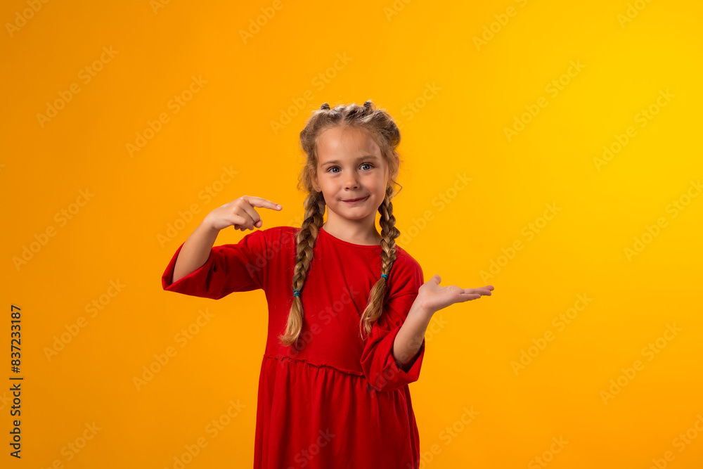 Smiling child girl pointing to an empty place on yellow background. Advertisement concept Smiling child girl pointing to an empty place on yellow background. Advertisement concept