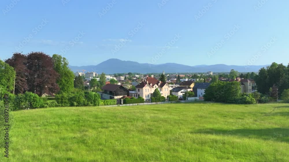 AERIAL: An imposing villa with an American flag flying in the wind boasts on a quiet, lush green street on the outskirts of the Ljubljana town, surrounded by the rising mountains in the background.