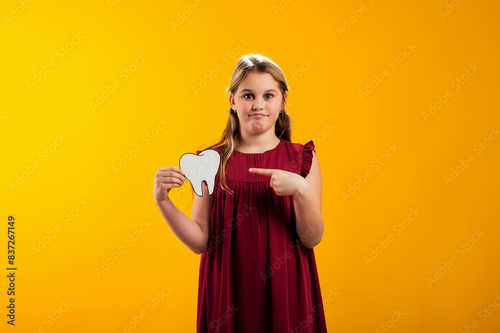 Smiling child girl holding papercraft tooth and pointing finger at it. Dental health concept Smiling child girl holding papercraft tooth and pointing finger at it. Dental health concept