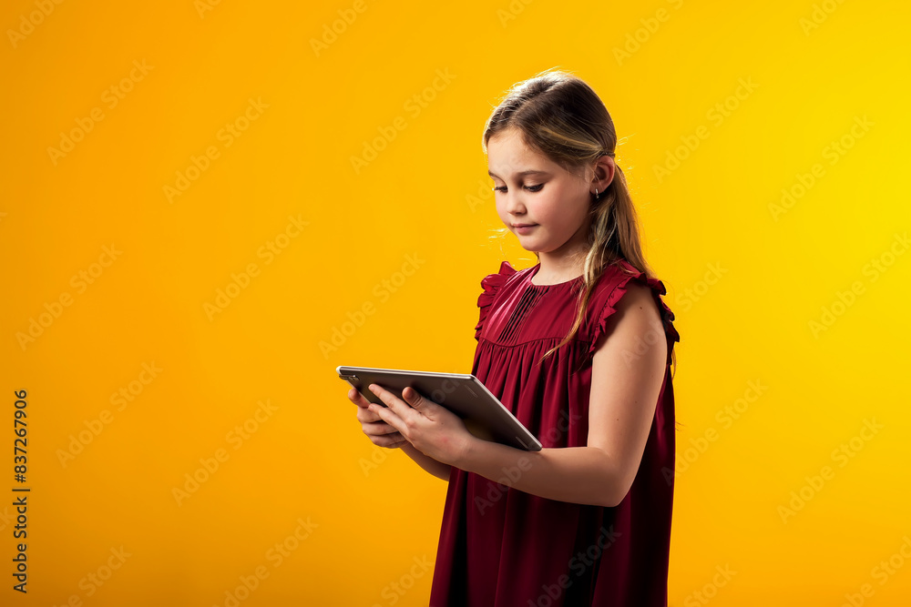 Smiling girl holding tablet in hand on yellow background. Lifestyle, leasure and gadget addiction concept Smiling girl holding tablet in hand on yellow background. Lifestyle, leasure and gadget addiction concept