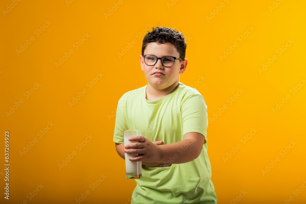 Kid boy holding glass of milk and feeling abdominal pain on yellow background. Lactose intolerance concept Kid boy holding glass of milk and feeling abdominal pain on yellow background. Lactose intolerance concept