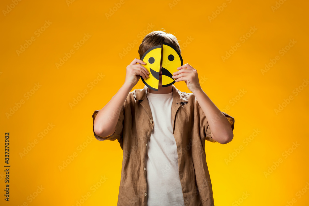 Boy holds emoticons with happy and sad emotions in front of face. Boy holds emoticons with happy and sad emotions in front of face.