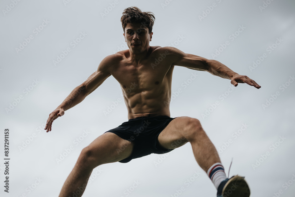 Obraz premium Shirtless man performing a high jump against a cloudy sky, demonstrating fitness, agility, and athleticism.