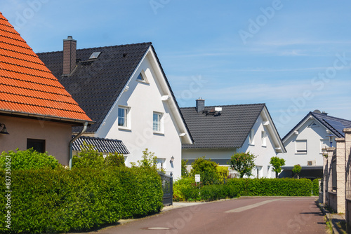 Fototapeta Naklejka Na Ścianę i Meble -  City street of single-family modern houses Germany against blue sky. German suburban small town residential area with row eco sustainable life building neighborhood suburb. Urban car parking driveway