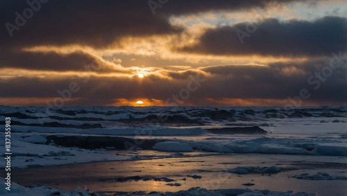 Winter s dawn breaks over a snowy seascape  dark clouds parting to reveal the rising sun.