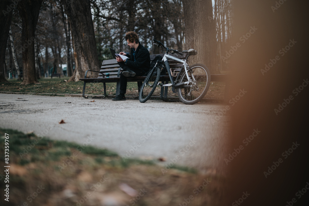 A business entrepreneur enjoys a peaceful moment reading while sitting on a park bench next to his bicycle.
