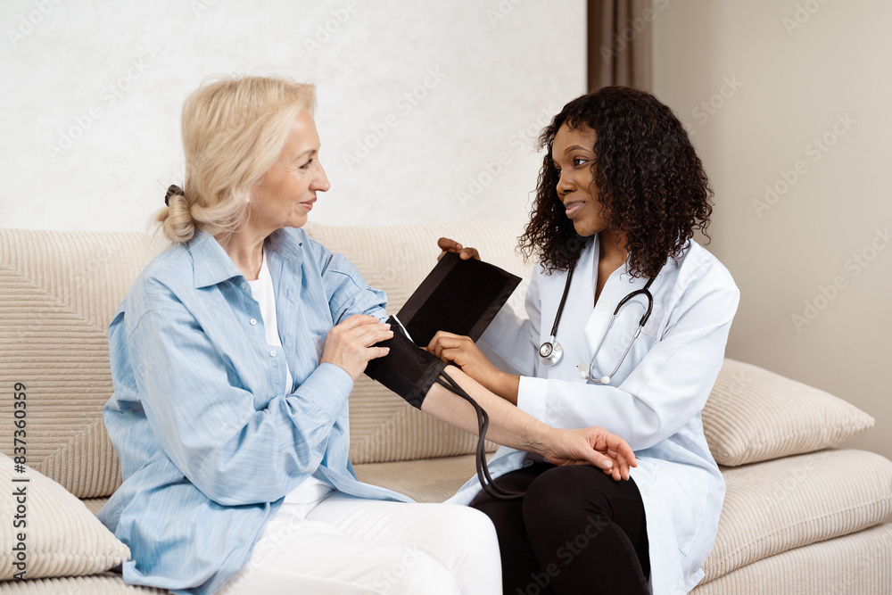 Friendly Female Doctor Measuring Elderly Patient's Blood Pressure In Cozy Home Setting Friendly Female Doctor Measuring Elderly Patient's Blood Pressure In Cozy Home Setting