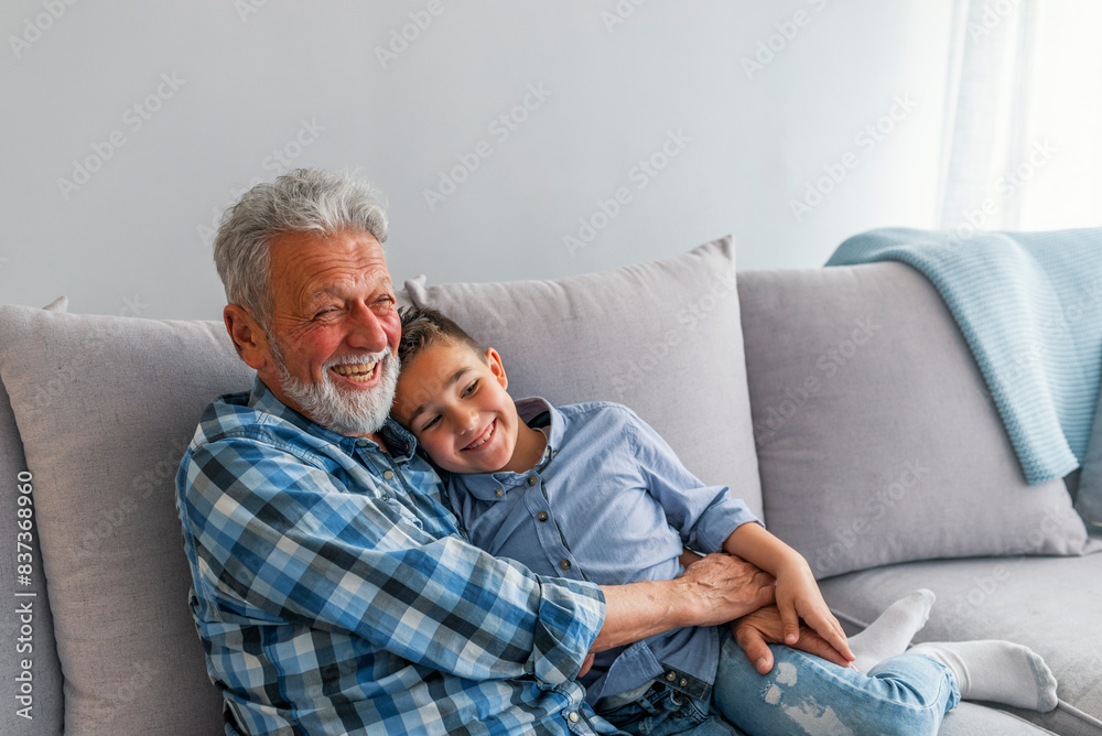 Grandfather and grandson playing and smiling at home. Grandfather hugging his grandson. Loving smiling grandparent and little boy child relax on sofa have close tender moment Grandfather and grandson playing and smiling at home. Grandfather hugging his grandson. Loving smiling grandparent and little boy child relax on sofa have close tender moment