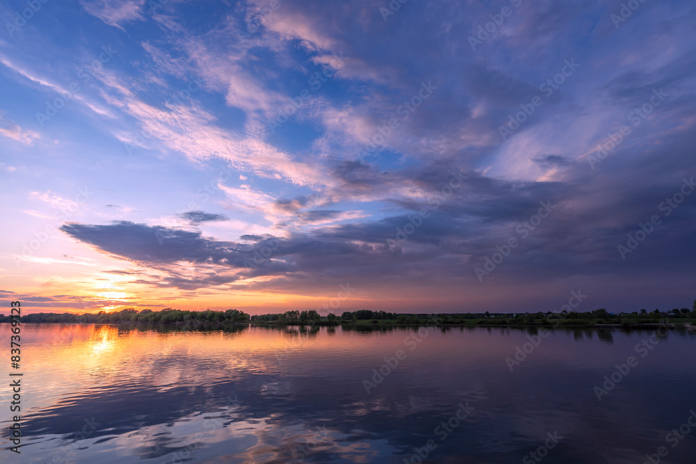 The sun is setting over the tranquil water, painting the sky with colorful clouds as it dips below the horizon. The sun is setting over the tranquil water, painting the sky with colorful clouds as it dips below the horizon.