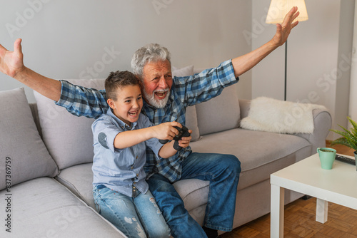 Tablou pe pânză Grandfather and grandson playing video game with console, happy time together