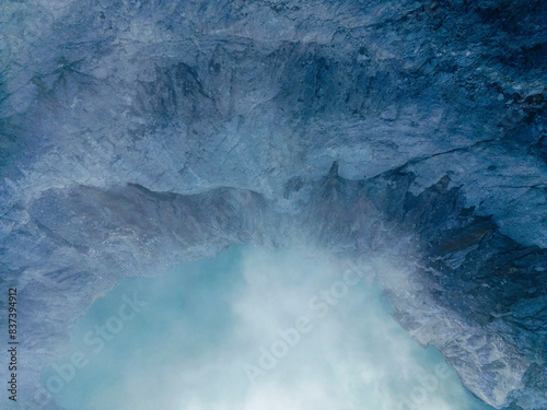 Top view of Ijen rocky mountain volcano with a crater hole in the middle  surrounded by grey clouds and fog