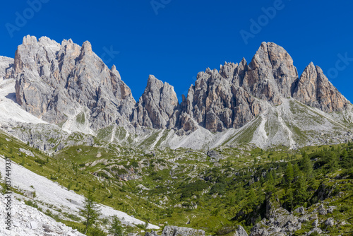 Dolomiti Alps beautiful mountain landscape. Rocky tower alpine summits in the Dolomites. Summer mountain scenic view on the hiking trekking path in the green mountain valley and blue sky with clouds