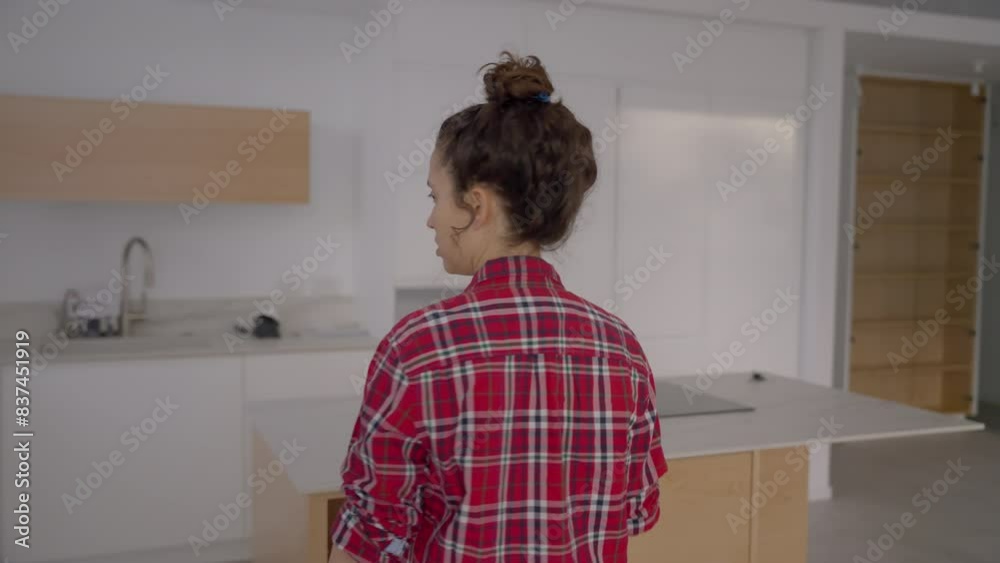 Young woman walking around new apartment smiling and visualizing her plans. Female designer or architect or new home owner envisioning the design in empty new home and kitchen with blank walls Young woman walking around new apartment smiling and visualizing her plans. Female designer or architect or new home owner envisioning the design in empty new home and kitchen with blank walls