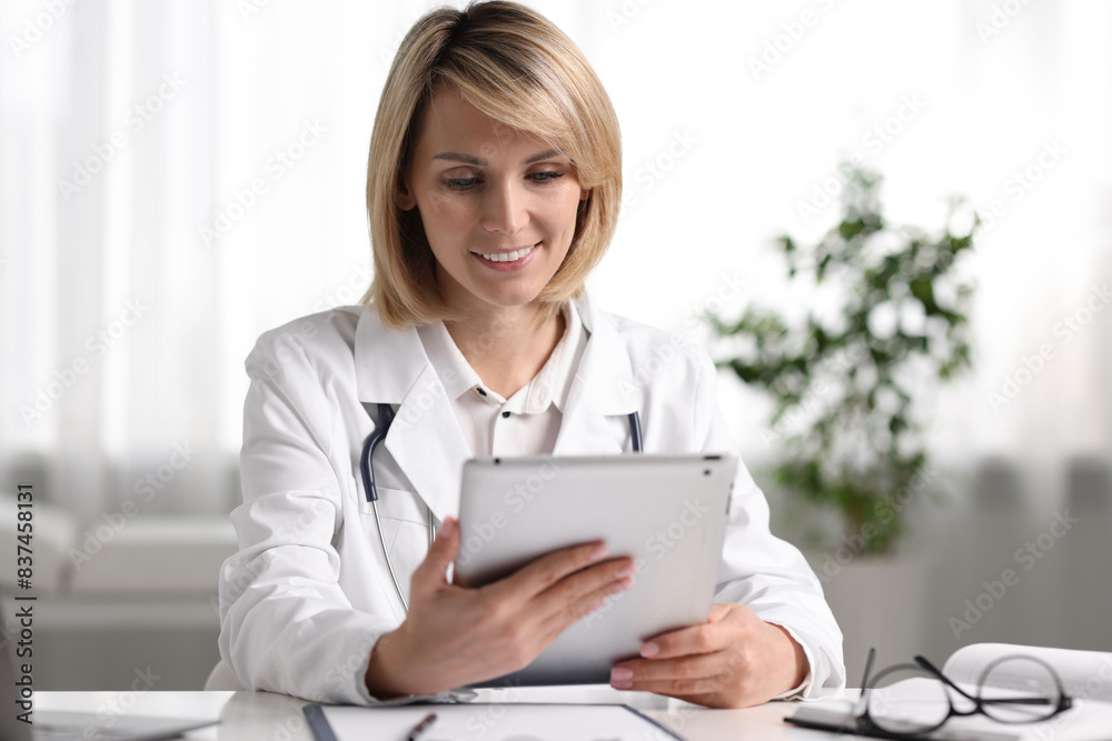 Smiling doctor with tablet having online consultation at table in office Smiling doctor with tablet having online consultation at table in office