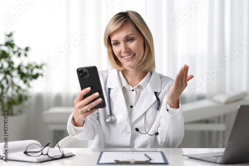 Smiling doctor with smartphone having online consultation at table in office © New Africa