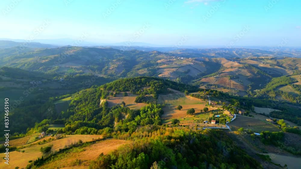 Pristine aerial pullback shot from Penna San Giovanni (MC) consisting of lush thickets, smooth wavy fields and meadows, roads, buildings, and hills as far as the eye can see, in typical Marche fashion