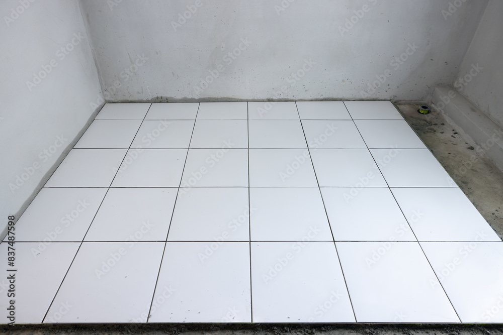 Fototapeta premium Tile floor under construction in perspective view by white square ceramic tile. Finishing material for interior, decoration, installation on concrete surface floor in bathroom, kitchen and shower room