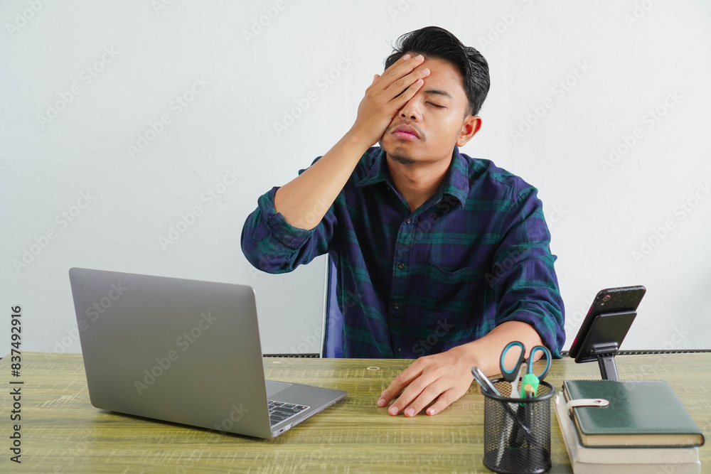 young asian man in blue shirt sit work at wooden desk with pc laptop isolated on white background. Achievement business career lifestyle concept. put palm on face, keeping eyes closed young asian man in blue shirt sit work at wooden desk with pc laptop isolated on white background. Achievement business career lifestyle concept. put palm on face, keeping eyes closed
