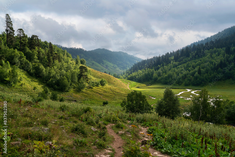 Naklejka premium The valley of the Malaya Dukka River surrounded by the mountains of the North Caucasus and the tourist trail to the Dukka Lakes on a sunny summer day, Arkhyz, Karachay-Cherkessia, Russia