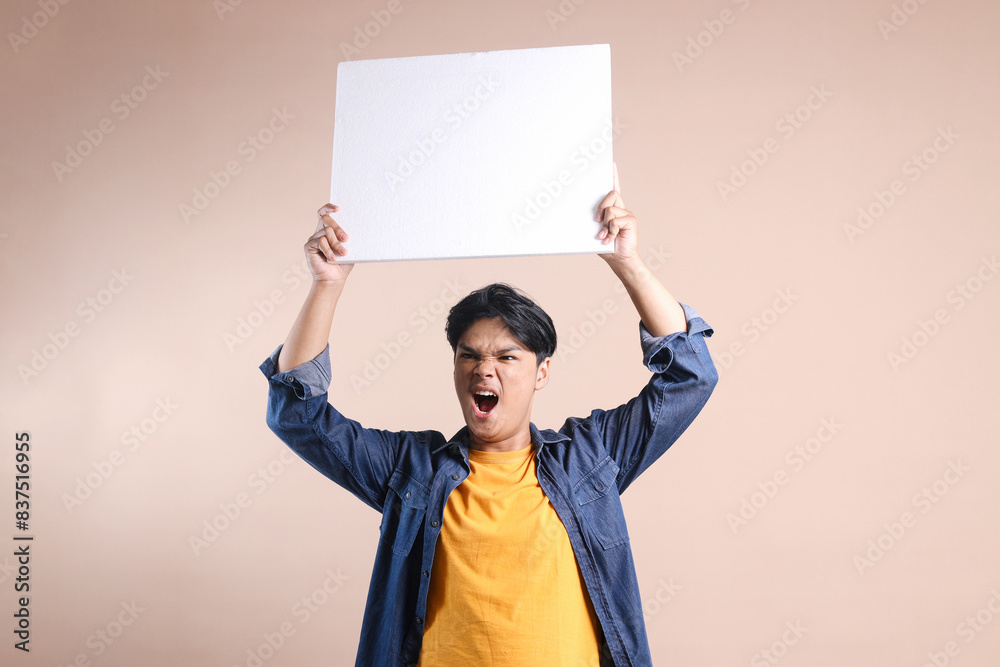 Potrait Of Excited Young Asian Man Raised The Placard For Mockup Isolated On Beige Background Potrait Of Excited Young Asian Man Raised The Placard For Mockup Isolated On Beige Background