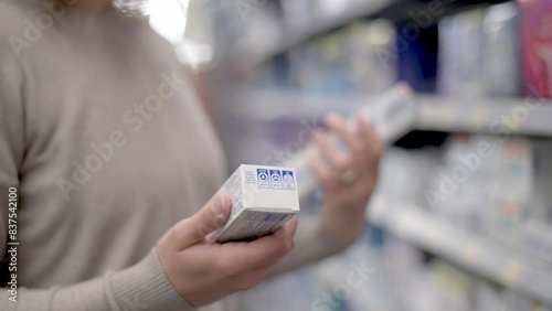 A woman examines two boxes of toothpaste in a store aisle, comparing them. The scene captures the act of decision-making in a retail environment.