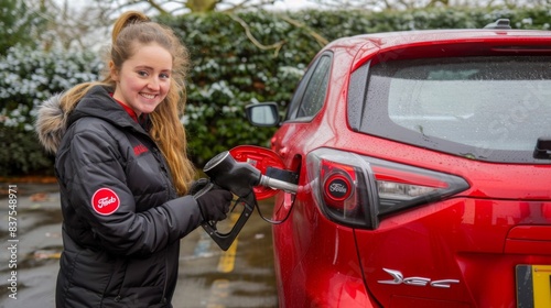 A woman is filling up a red car with gas