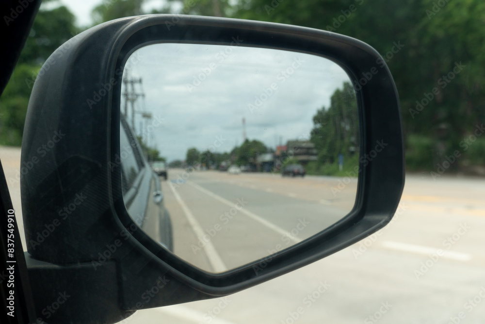 Inside view of mirrors wing. Rear view of a gray car with asphalt road and green trees with small city in the daytime. Clear traffic in rural areas. Inside view of mirrors wing. Rear view of a gray car with asphalt road and green trees with small city in the daytime. Clear traffic in rural areas.
