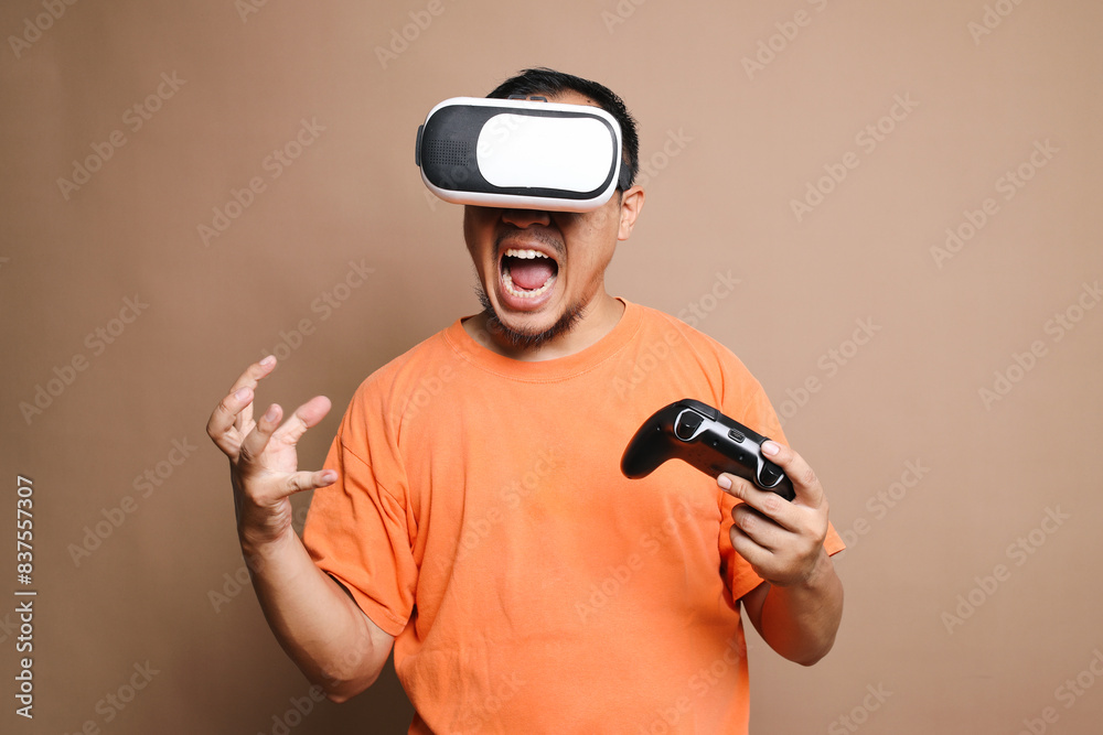 Angry Asian guy using VR goggles and joystick losing video games isolated on beige background Angry Asian guy using VR goggles and joystick losing video games isolated on beige background