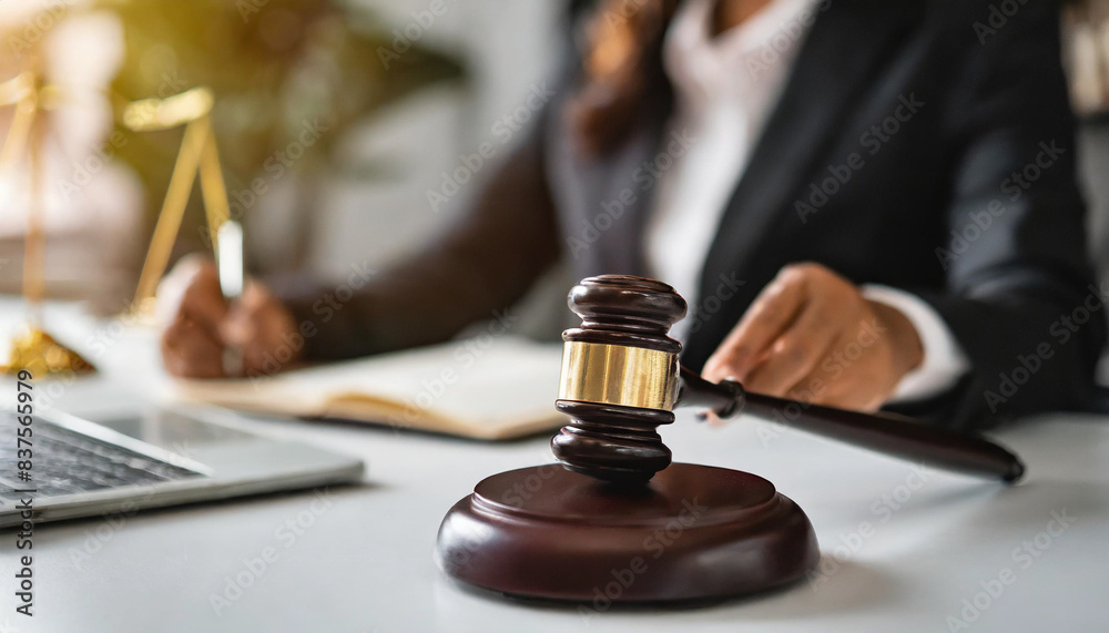 wooden judge's gavel and block on a white table symbolize justice and authority, with a blurred lawyer's hand in the office background, representing legal work and the judicial process wooden judge's gavel and block on a white table symbolize justice and authority, with a blurred lawyer's hand in the office background, representing legal work and the judicial process