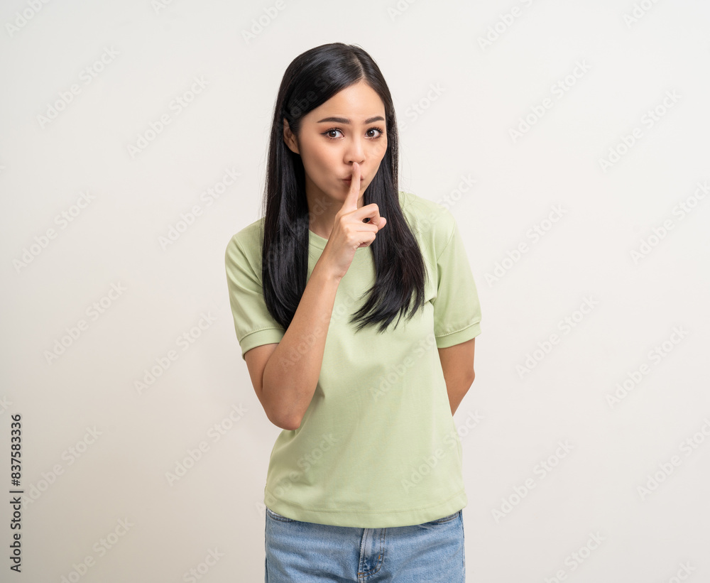 Happy beautiful young asian woman whispering some secret gossip. Excited pretty latin girl index finger on mouth standing pose on isolated white background. Happy beautiful young asian woman whispering some secret gossip. Excited pretty latin girl index finger on mouth standing pose on isolated white background.