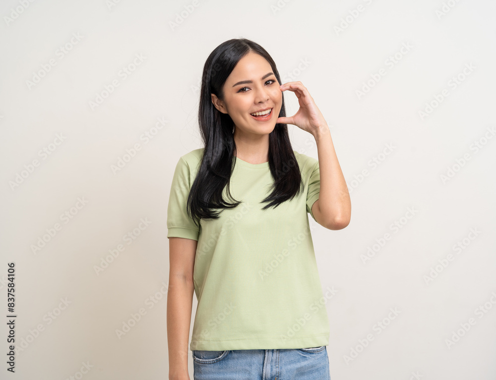 Pretty Young beautiful Asian woman standing and smiling showing mini heart sign on cheek with isolated white background. Lovely Latin female wearing green shirt feeling surprised and happy. Pretty Young beautiful Asian woman standing and smiling showing mini heart sign on cheek with isolated white background. Lovely Latin female wearing green shirt feeling surprised and happy.