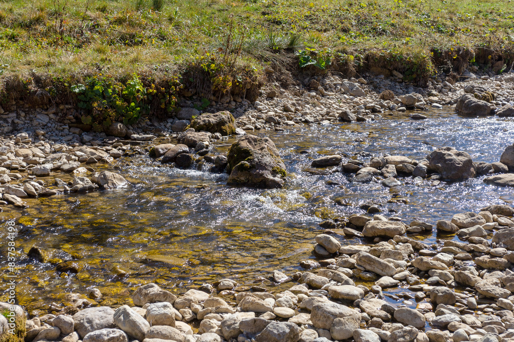 Shallow riverbed with a rocky bottom , unhurried flow of water, autumn walks in nature Shallow riverbed with a rocky bottom , unhurried flow of water, autumn walks in nature