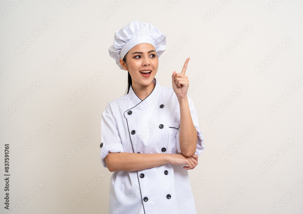 Smiling Young beautiful asian woman chef in uniform pointing finger to copy space isolated background. Cooking woman Occupation chef or baker People in kitchen restaurant and hotel.