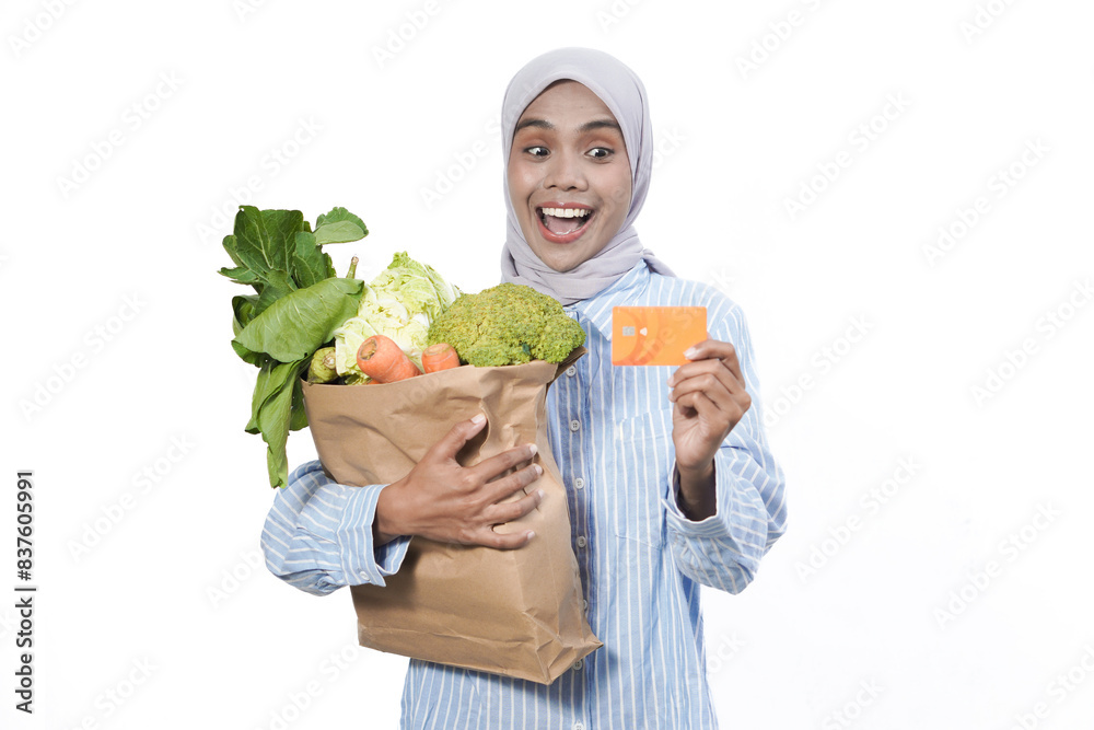 Young woman wear casual clothes hold brown paper bag with vegetable products mock up of credit bank card isolated on white background studio portrait Young woman wear casual clothes hold brown paper bag with vegetable products mock up of credit bank card isolated on white background studio portrait