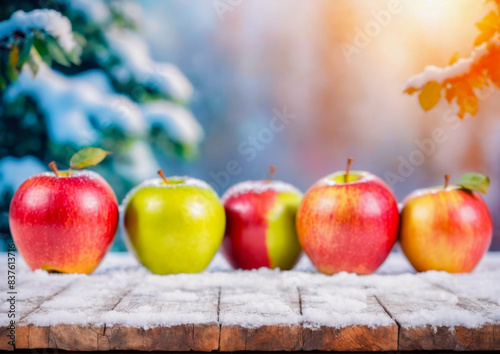 Colorful apples lay on a wooden table covered with snow. Apples lay on the wooden floor and were covered with snow. © Naluphon