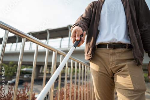 Young blind man walking in city with walking stick. Visually impaired man difficult to traveling on the road wearing sun glasses Cross the road cross the footbridge