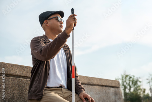 Quadro em tela Young asian blind man sitting outside holding walking stick Visually impaired ma