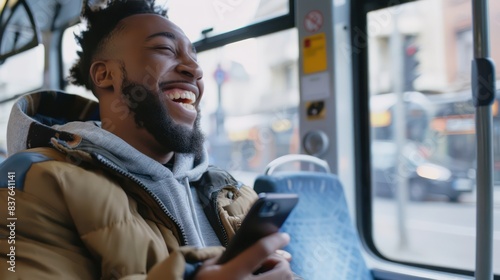 A candid photo of a handsome young man laughing at something on his smartphone screen while on the bus. 