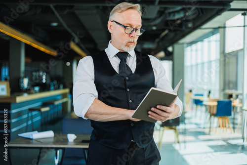 Male financier with gray hair reviewing financial reports and contracts, adult boss working with papers at office workplace.